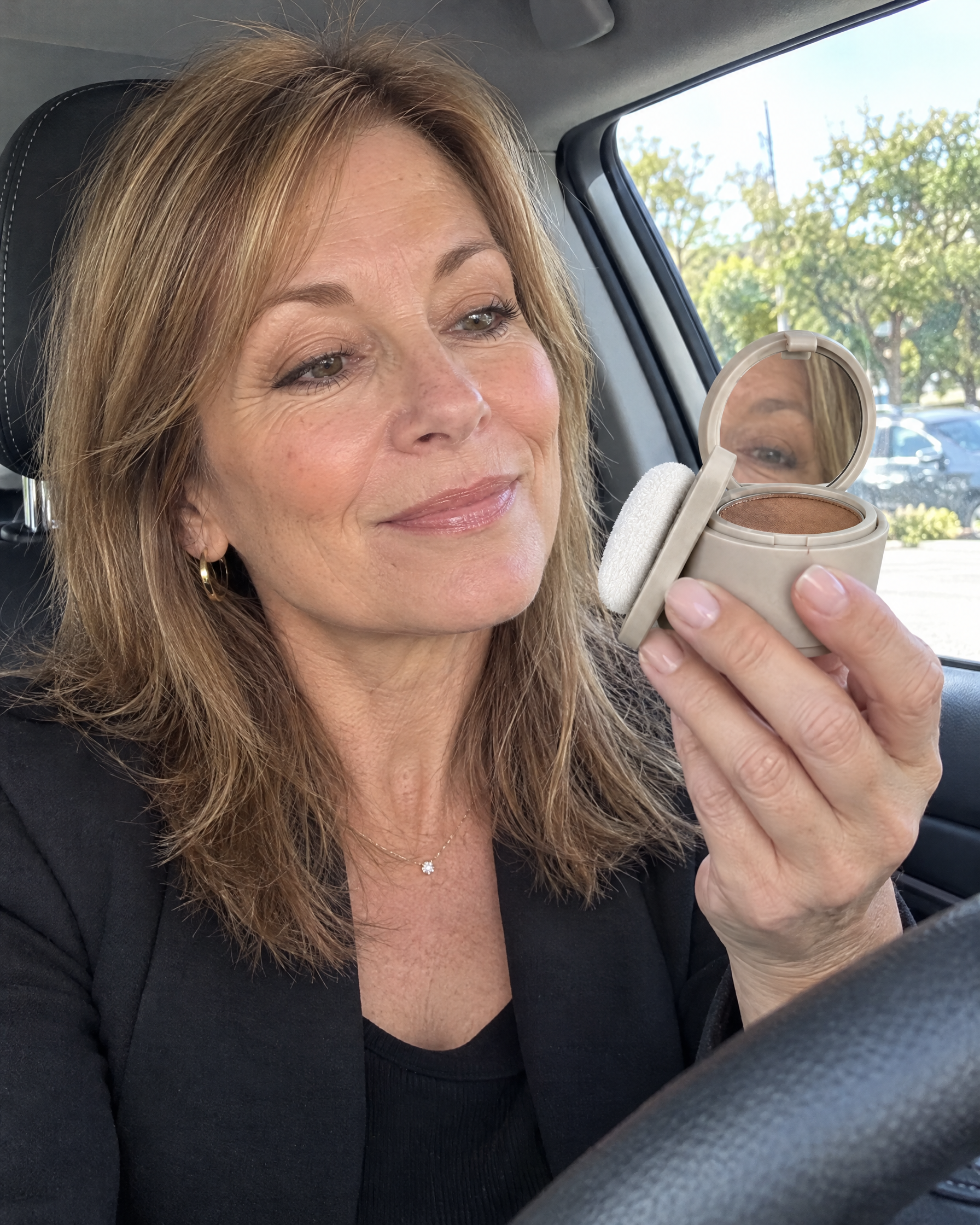 Woman checking her part in the compact mirror in her car